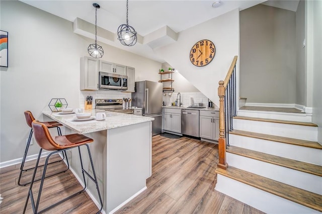 kitchen with appliances with stainless steel finishes, decorative light fixtures, backsplash, and light wood finished floors