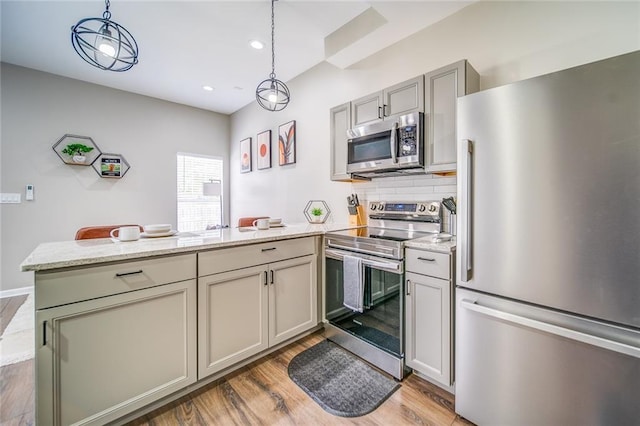 kitchen featuring light wood-style flooring, stainless steel appliances, a peninsula, backsplash, and decorative light fixtures