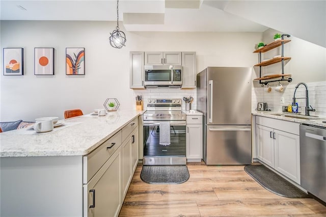 kitchen with light wood finished floors, appliances with stainless steel finishes, a peninsula, open shelves, and a sink