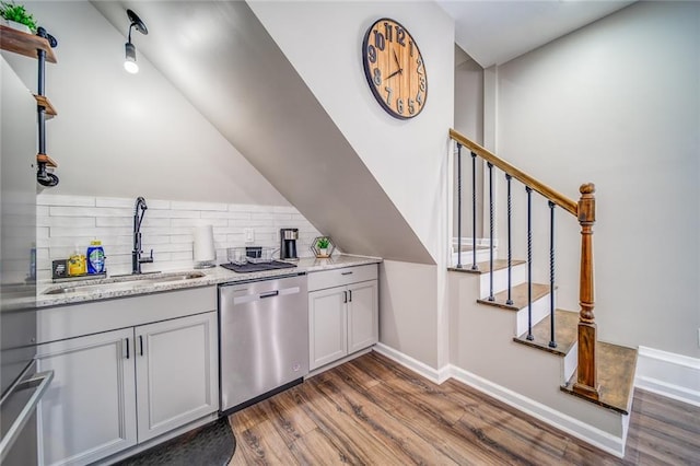 kitchen with dishwasher, dark wood-style floors, light stone counters, backsplash, and a sink