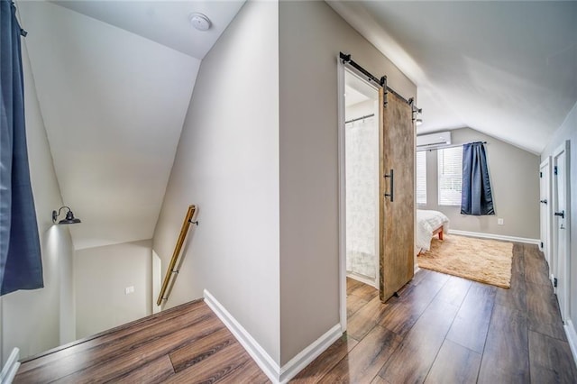 interior space featuring a barn door, baseboards, lofted ceiling, dark wood-type flooring, and an upstairs landing