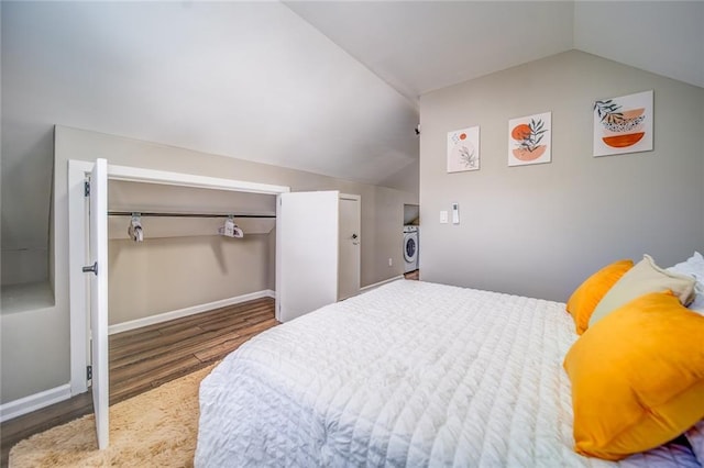 bedroom with washer / dryer, vaulted ceiling, baseboards, and wood finished floors