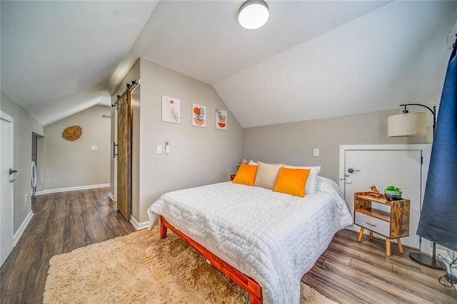 bedroom with lofted ceiling, a barn door, baseboards, and wood finished floors