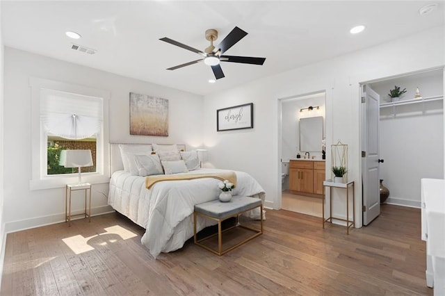 bedroom featuring wood finished floors, baseboards, a walk in closet, recessed lighting, and ensuite bath
