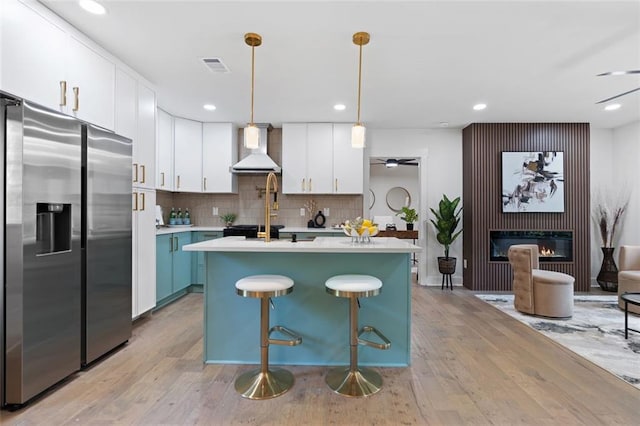 kitchen featuring stainless steel refrigerator with ice dispenser, wall chimney exhaust hood, light wood-style flooring, light countertops, and white cabinetry
