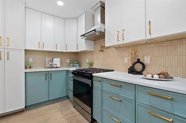 kitchen featuring stainless steel gas range, wall chimney range hood, light countertops, decorative backsplash, and blue cabinets