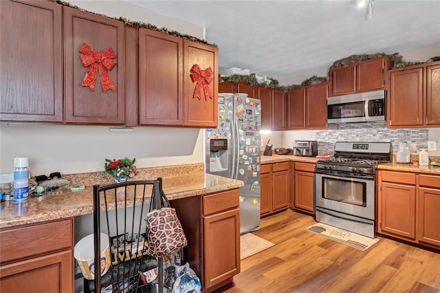 kitchen featuring light stone countertops, appliances with stainless steel finishes, tasteful backsplash, and light hardwood / wood-style flooring