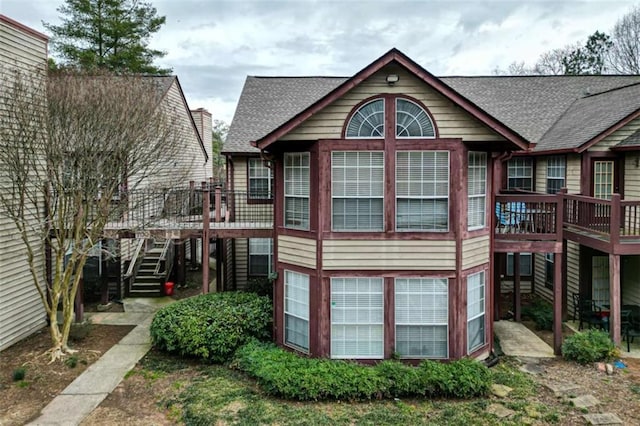 rear view of property with a deck, stairs, and roof with shingles