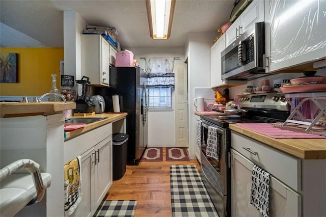 kitchen with white cabinets, appliances with stainless steel finishes, light wood-type flooring, and a sink