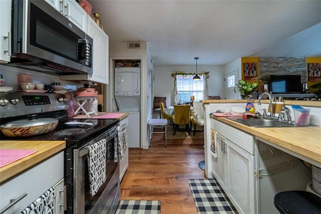 kitchen featuring stacked washing maching and dryer, white cabinets, stainless steel appliances, wood counters, and a sink