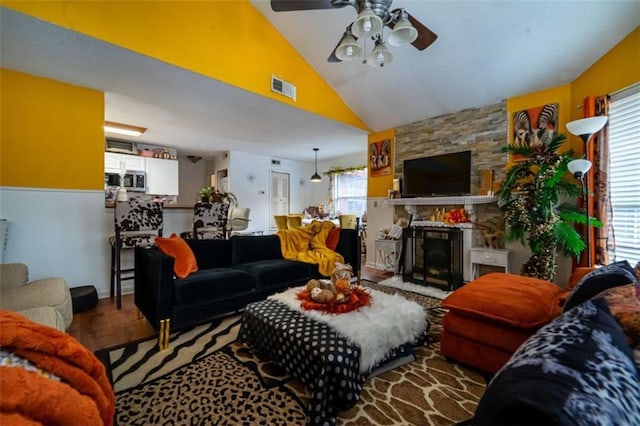 living area with visible vents, wood finished floors, a stone fireplace, ceiling fan, and vaulted ceiling