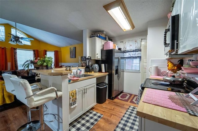 kitchen with a breakfast bar area, light wood-style flooring, appliances with stainless steel finishes, a peninsula, and a sink