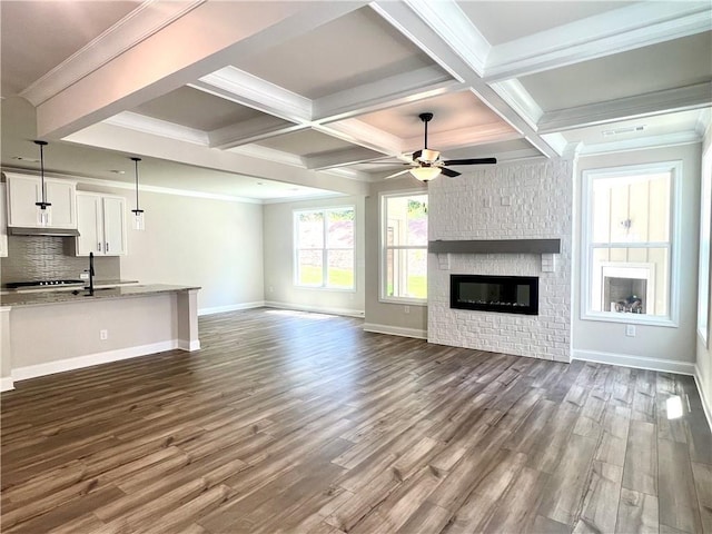 unfurnished living room featuring a brick fireplace, coffered ceiling, ceiling fan, dark wood-type flooring, and beamed ceiling