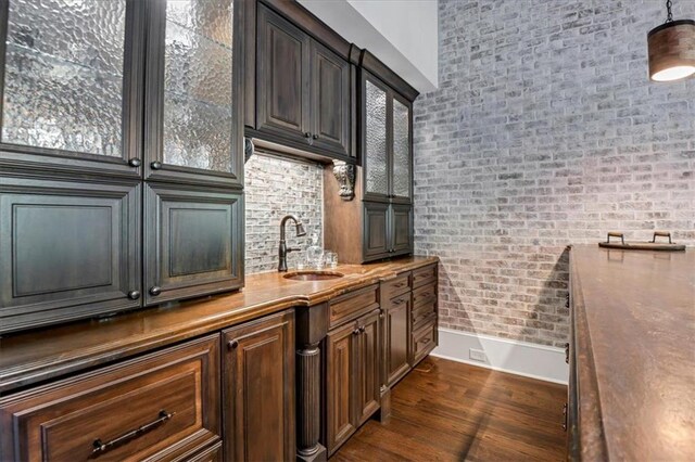 kitchen featuring sink, dark brown cabinets, dark hardwood / wood-style floors, and brick wall