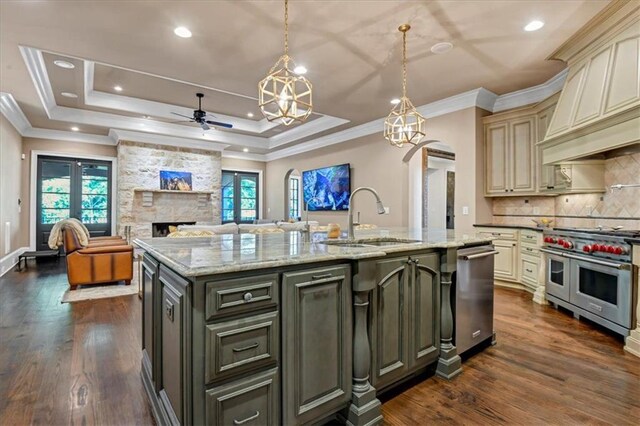 kitchen featuring appliances with stainless steel finishes, decorative backsplash, a center island with sink, a raised ceiling, and cream cabinets