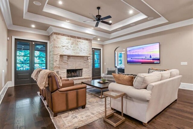 living room featuring a stone fireplace, dark wood-type flooring, and a tray ceiling