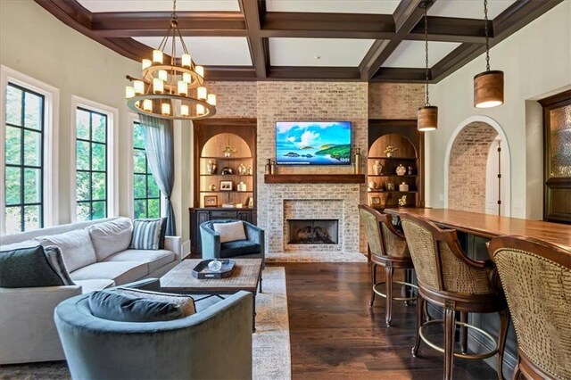 living room with an inviting chandelier, built in shelves, coffered ceiling, a fireplace, and dark wood-type flooring