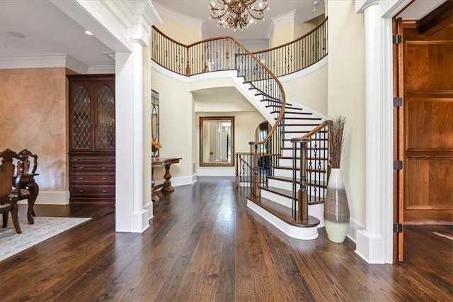 foyer with a high ceiling, a notable chandelier, dark hardwood / wood-style flooring, crown molding, and decorative columns