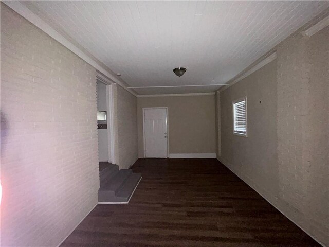 corridor with ornamental molding, dark wood-type flooring, and brick wall