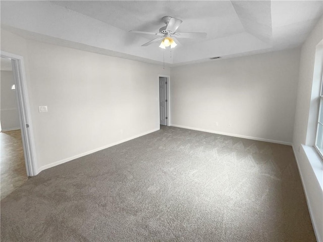 empty room featuring a raised ceiling, dark carpet, and baseboards