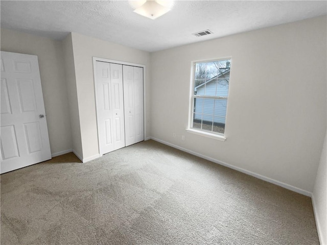 unfurnished bedroom with a textured ceiling, carpet flooring, visible vents, baseboards, and a closet
