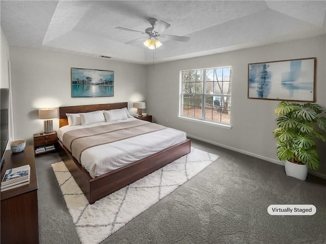 carpeted bedroom featuring a textured ceiling, ceiling fan, visible vents, baseboards, and a raised ceiling