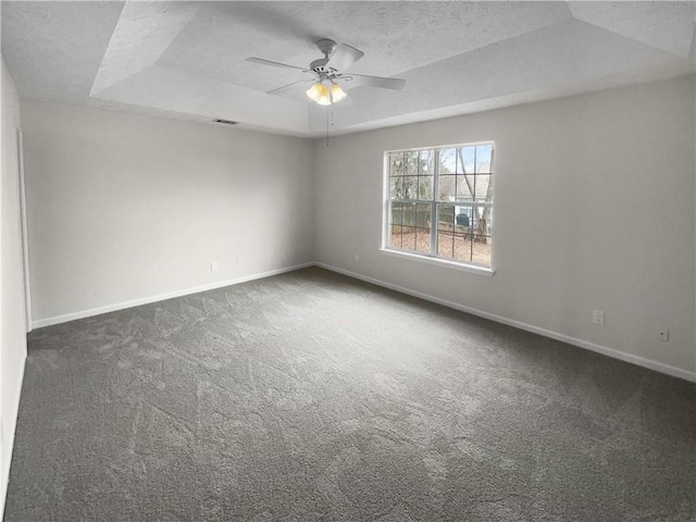 empty room with dark colored carpet, a raised ceiling, a textured ceiling, and baseboards