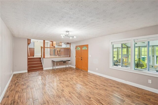 2201 Colonial Oak Way, Stone Mountain, GA 30087 - unfurnished living room with wood finished floors, a chandelier, stairway, a textured ceiling, and baseboards