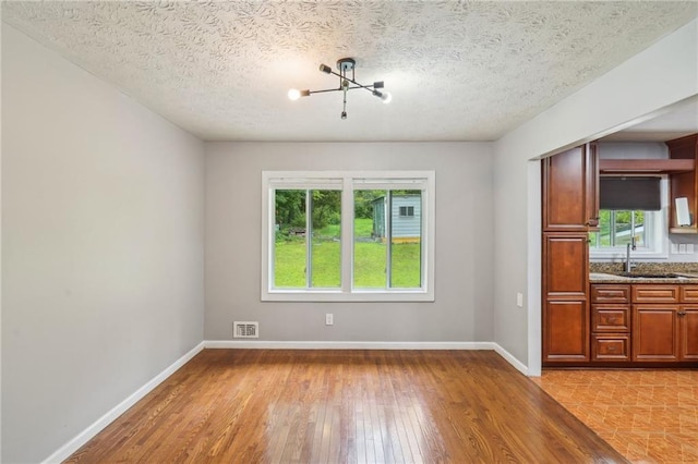 2201 Colonial Oak Way, Stone Mountain, GA 30087 - unfurnished dining area featuring a chandelier, light wood finished floors, a sink, baseboards, and a textured ceiling
