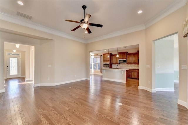 unfurnished living room with ceiling fan, a wealth of natural light, ornamental molding, and hardwood / wood-style floors