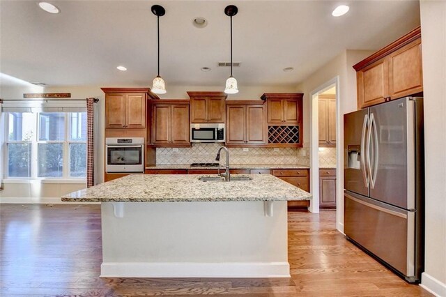 kitchen with appliances with stainless steel finishes, a sink, light stone countertops, and decorative backsplash