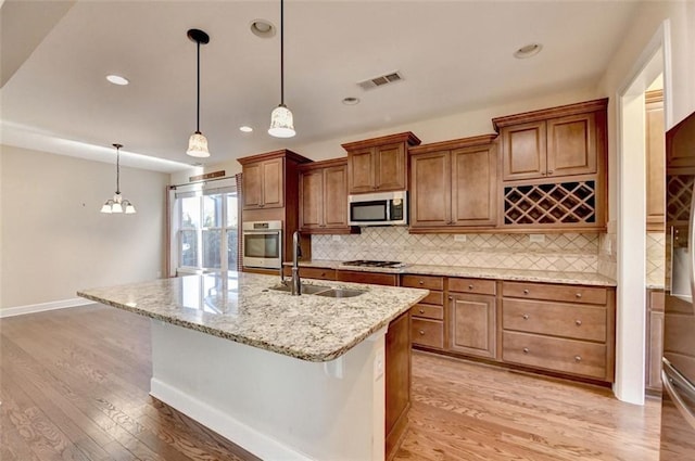 kitchen featuring appliances with stainless steel finishes, decorative light fixtures, sink, a kitchen island with sink, and a breakfast bar area