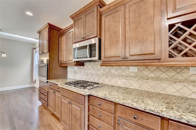 kitchen featuring baseboards, decorative backsplash, appliances with stainless steel finishes, light stone countertops, and light wood-type flooring