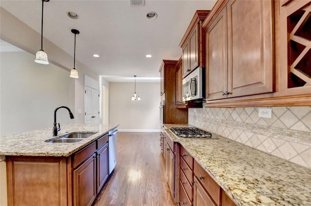 kitchen with appliances with stainless steel finishes, tasteful backsplash, a kitchen island with sink, sink, and pendant lighting