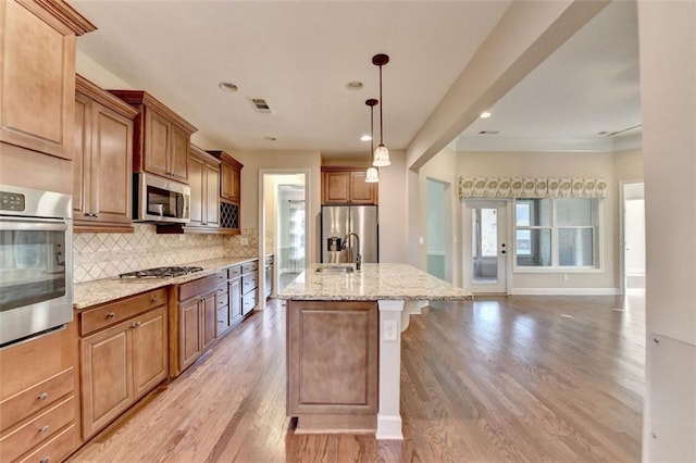 kitchen with light stone counters, stainless steel appliances, visible vents, light wood-style floors, and decorative backsplash