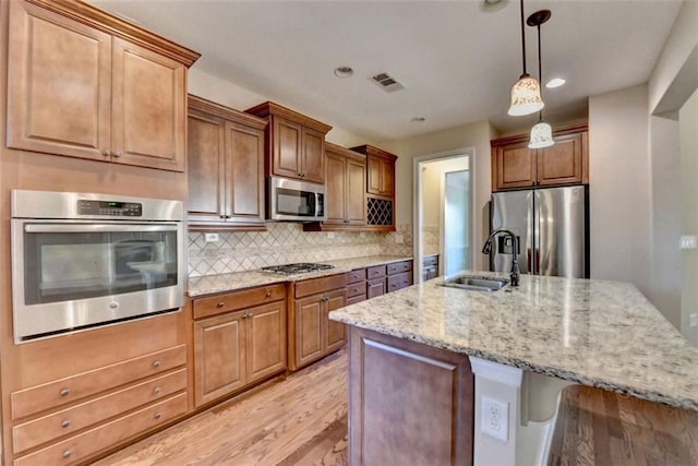 kitchen with appliances with stainless steel finishes, hanging light fixtures, sink, backsplash, and an island with sink