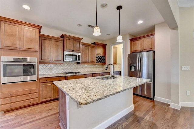 kitchen with pendant lighting, appliances with stainless steel finishes, sink, backsplash, and a kitchen island with sink