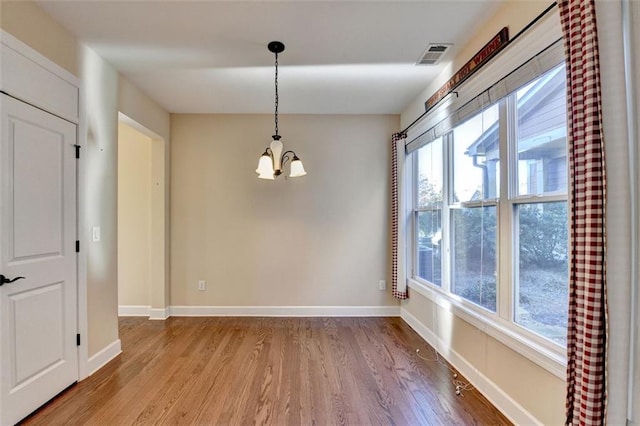 empty room with light wood-type flooring, a wealth of natural light, and a notable chandelier