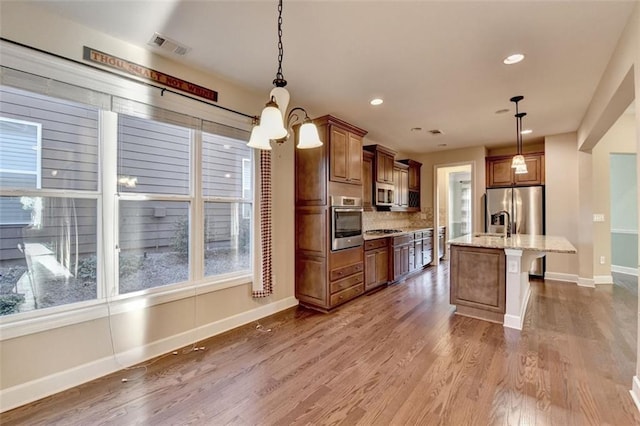 kitchen with wood finished floors, appliances with stainless steel finishes, brown cabinetry, light stone countertops, and baseboards