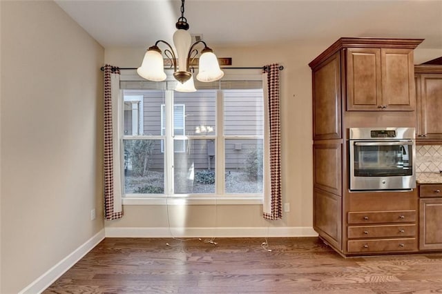 kitchen with hanging light fixtures, dark wood-type flooring, decorative backsplash, stainless steel oven, and a chandelier