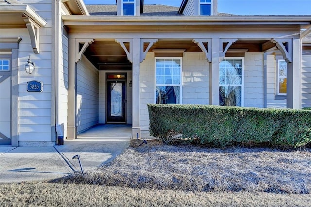 property entrance featuring covered porch and a shingled roof