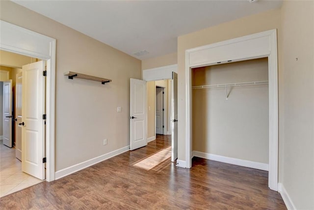 unfurnished bedroom featuring a closet, wood finished floors, visible vents, and baseboards