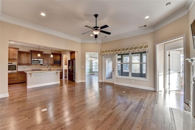 unfurnished living room featuring ceiling fan, sink, wood-type flooring, and crown molding