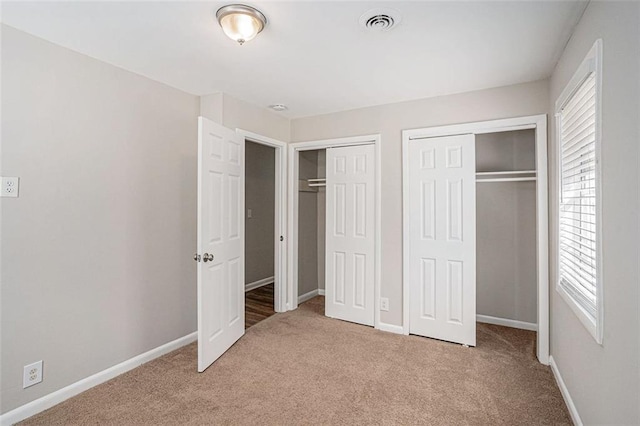 unfurnished bedroom featuring baseboards, light colored carpet, visible vents, and multiple closets