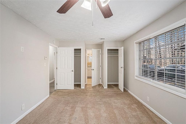 unfurnished bedroom featuring a textured ceiling, light colored carpet, a ceiling fan, baseboards, and multiple closets