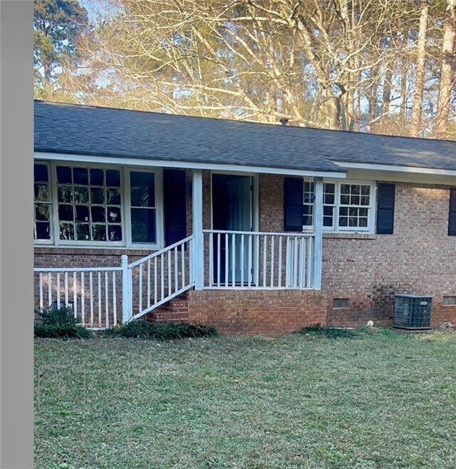 view of front of property with covered porch, a front yard, and central air condition unit