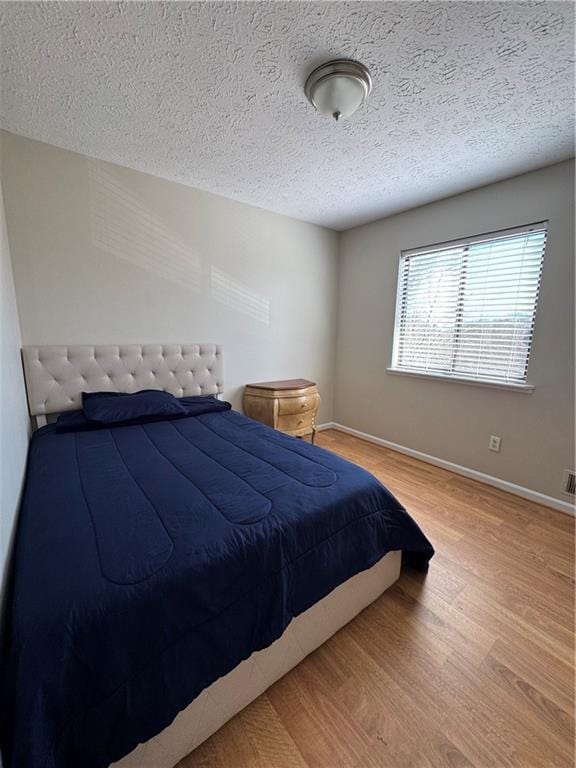 bedroom featuring a textured ceiling, baseboards, and wood finished floors