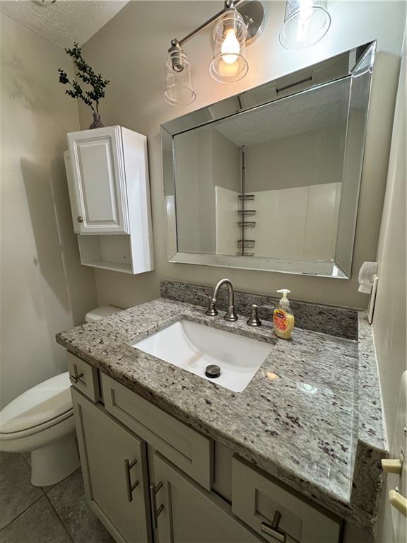 bathroom featuring a textured ceiling, vanity, toilet, and tile patterned floors