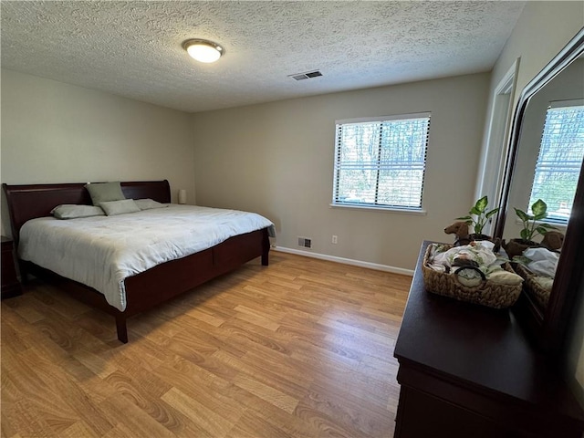 bedroom featuring baseboards, visible vents, light wood finished floors, and multiple windows