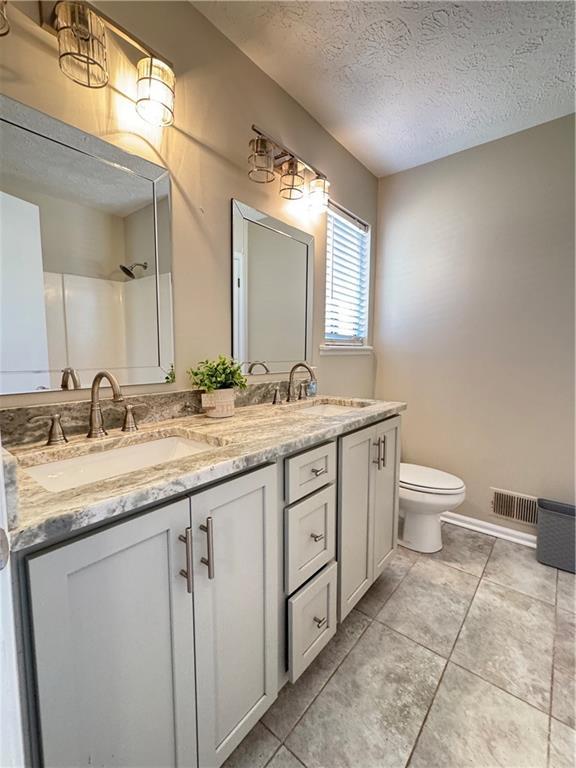 bathroom featuring toilet, double vanity, a textured ceiling, and a sink